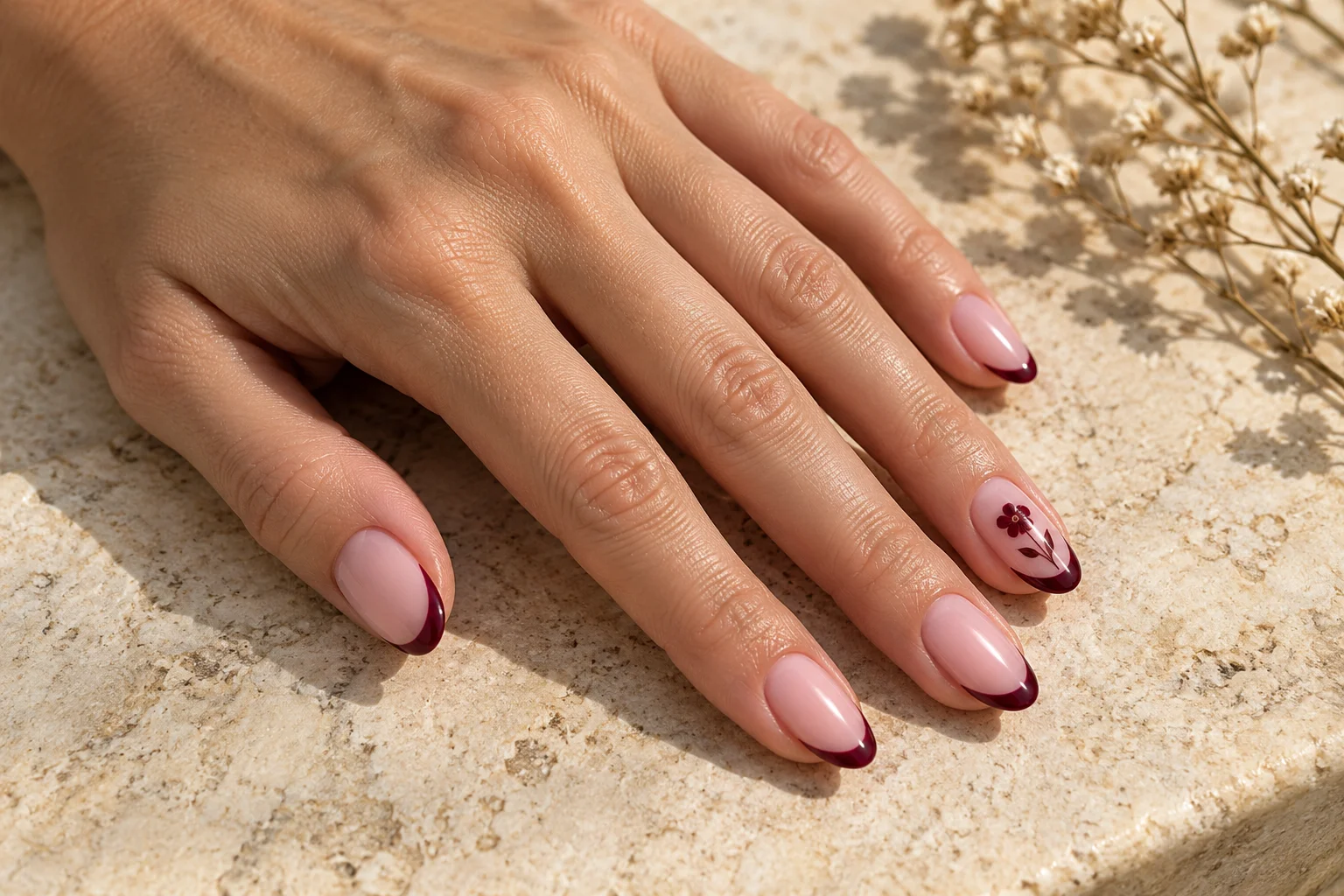 Blush almond nails with burgundy French tips and a delicate floral accent