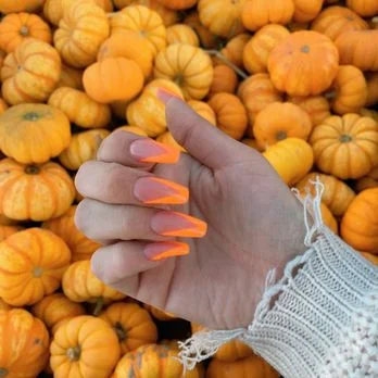 Orange manicure with autumn accents photographed beside pumpkins